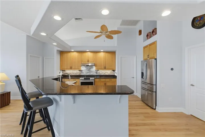 Kitchen with dark stone countertops, stainless steel appliances, light wood-style floors, a kitchen bar, and backsplash