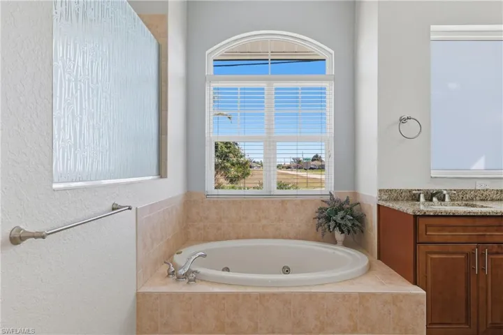 Full bathroom featuring a whirlpool tub, a textured wall, and vanity