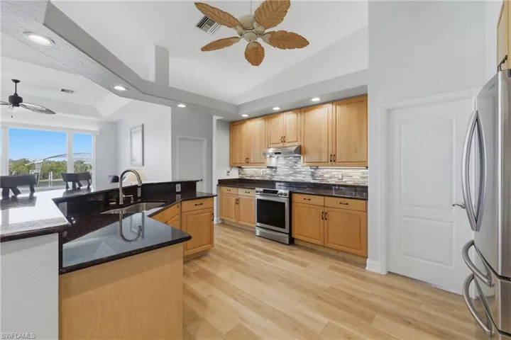 Kitchen with a ceiling fan, stainless steel appliances, light wood-style flooring, backsplash, and dark stone counters