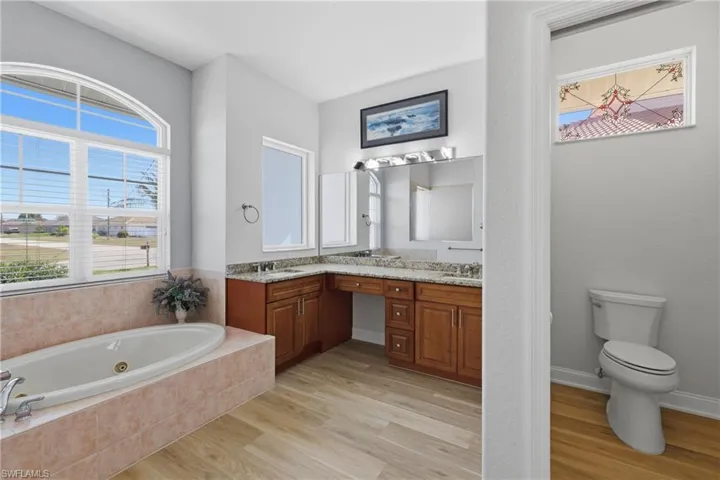 Full bath with double vanity, a whirlpool tub, and light wood-style floors
