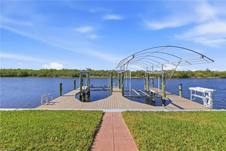 Dock with boat lift, a lawn, and a water view