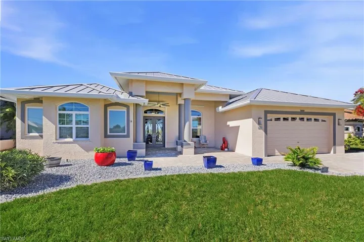 Front of home featuring a standing seam roof, french doors, a front lawn, and stucco siding, paver driveway