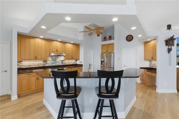 Kitchen with backsplash, a breakfast bar area, stainless steel fridge with ice dispenser, dark stone counters, and light wood-type flooring