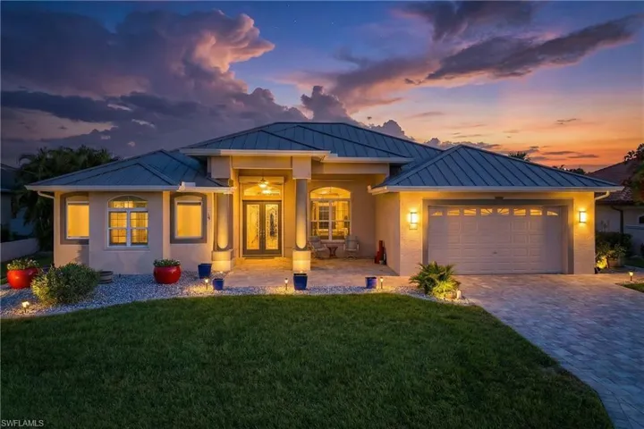 View of front of house featuring a standing seam roof, a lawn, decorative driveway, and an attached garage