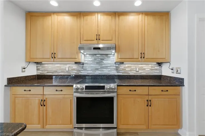 Kitchen with stainless steel range with electric stovetop, dark stone counters, and backsplash