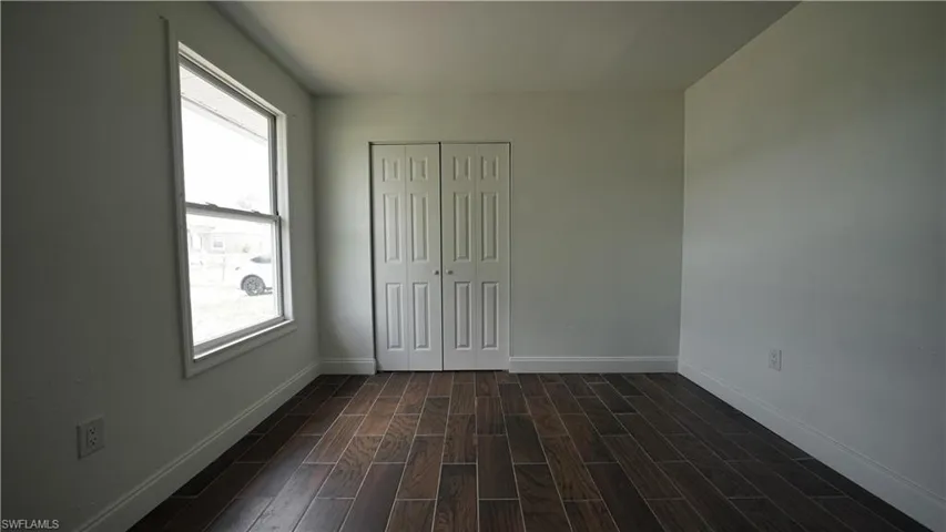 Unfurnished bedroom with dark wood finished floors, baseboards, and a closet