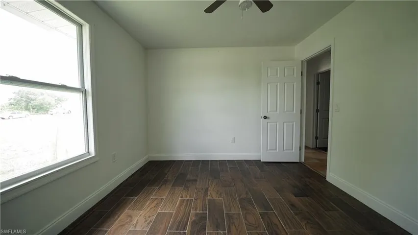 Spare room with ceiling fan, dark wood-style flooring, and baseboards
