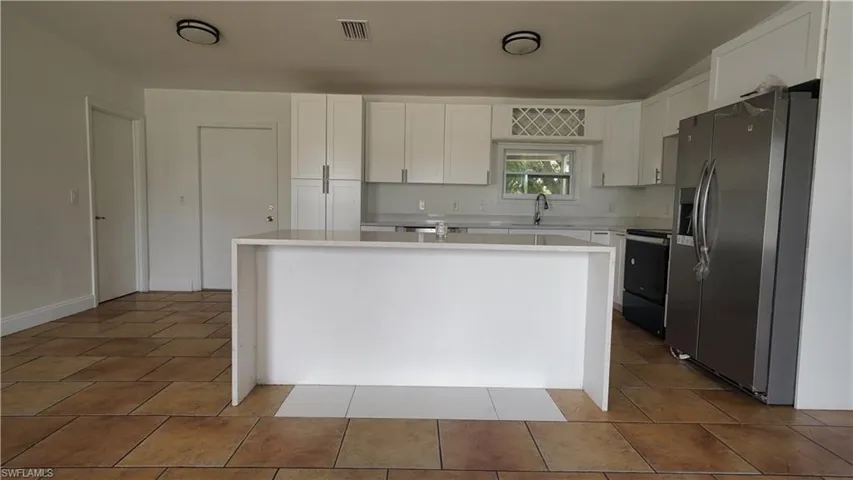 Kitchen featuring stainless steel fridge with ice dispenser, light countertops, white cabinets, electric range, and a sink