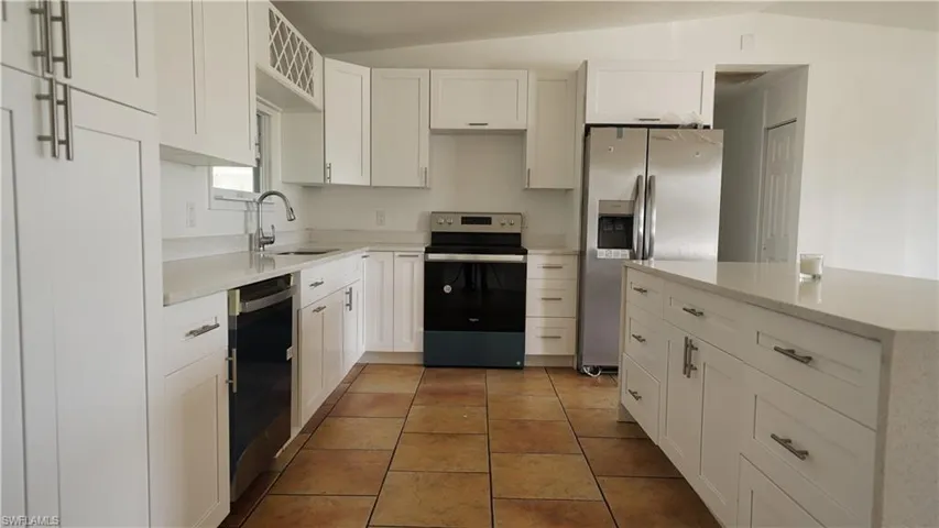 Kitchen featuring stainless steel appliances, a sink, white cabinets, light countertops, and a kitchen island