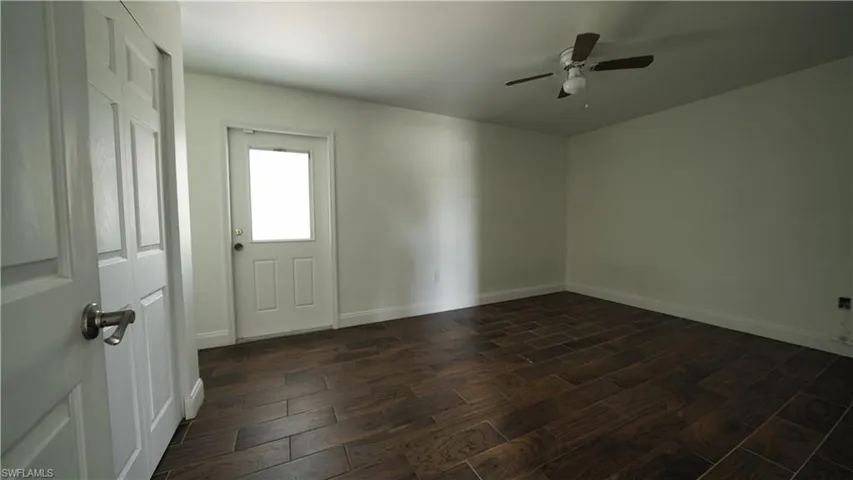 Empty room featuring dark wood-style flooring, ceiling fan, and baseboards