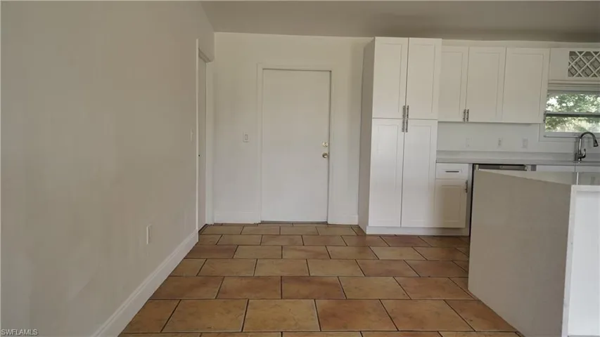 Kitchen with light countertops, white cabinetry, a sink, tile patterned flooring, and baseboards
