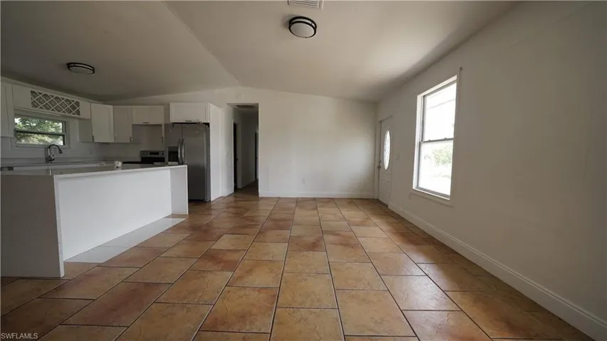 Kitchen with vaulted ceiling, stainless steel appliances, white cabinetry, light countertops, and baseboards