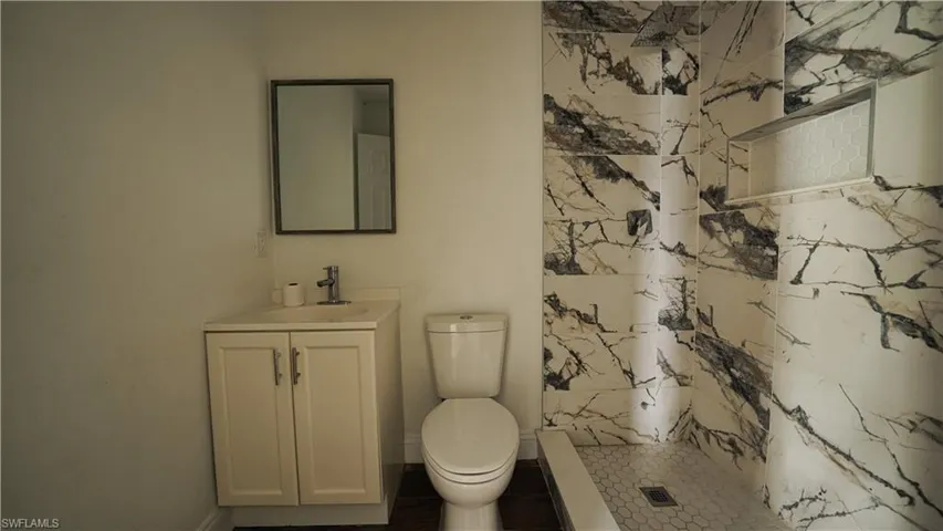 Bathroom featuring a stall shower, vanity, toilet, and baseboards