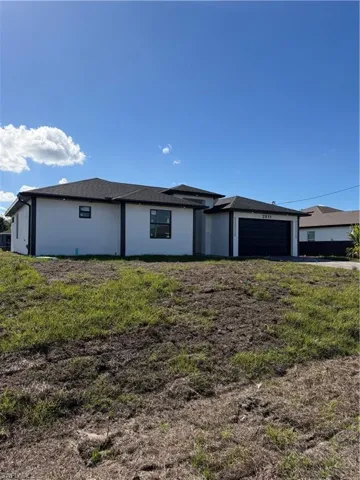 View of front of house with stucco siding, a garage, and a front lawn