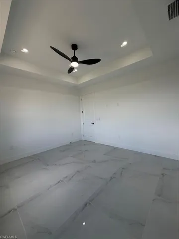 Unfurnished room with a raised ceiling, recessed lighting, ceiling fan, and marble finish flooring