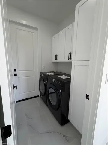 Washroom with cabinet space, light marble finish flooring, and washing machine and dryer