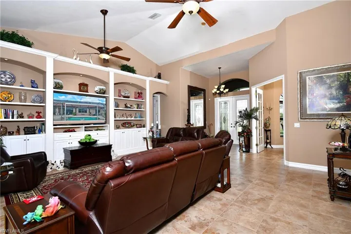 Tiled living room featuring ceiling fan with notable chandelier, vaulted ceiling, built in shelves, and french doors