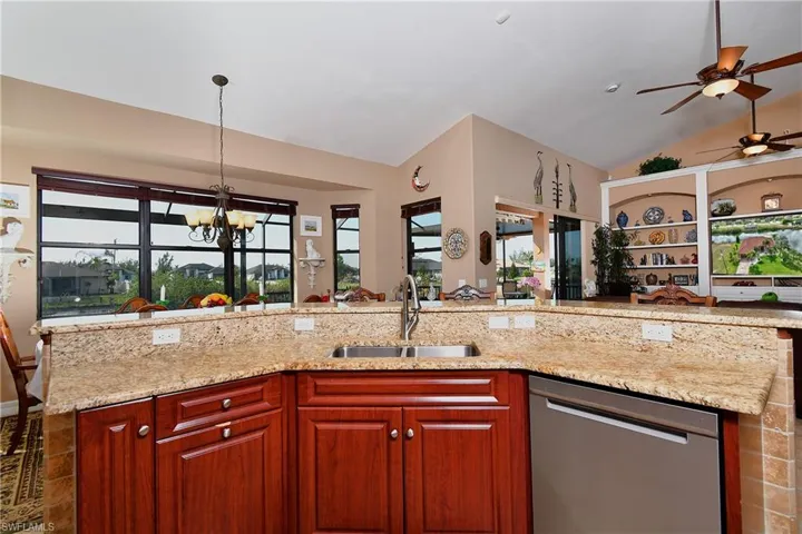 Kitchen with hanging light fixtures, dishwasher, light stone counters, vaulted ceiling, and sink