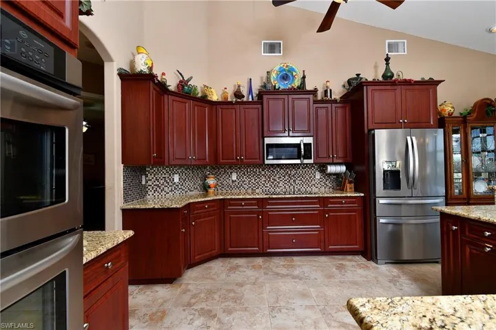 Kitchen with high vaulted ceiling, ceiling fan, light stone counters, appliances with stainless steel finishes, and decorative backsplash