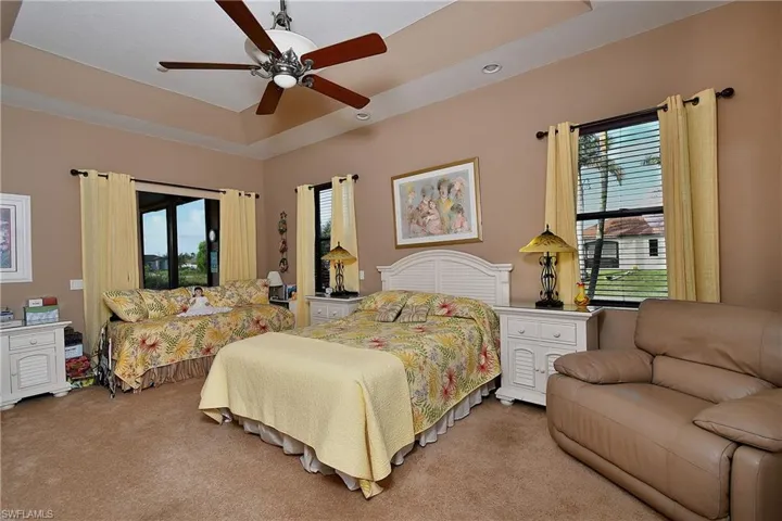 Carpeted bedroom with multiple windows, ceiling fan, access to outside, and a tray ceiling