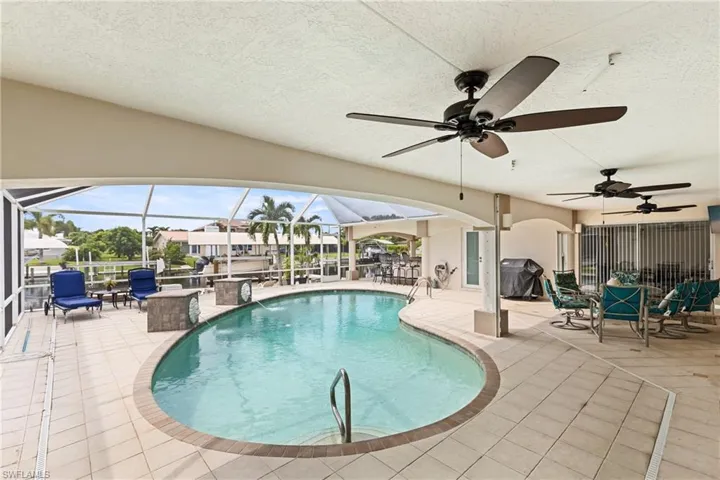 Outdoor pool featuring a patio area, a sunroom, grilling area, a ceiling fan, and glass enclosure