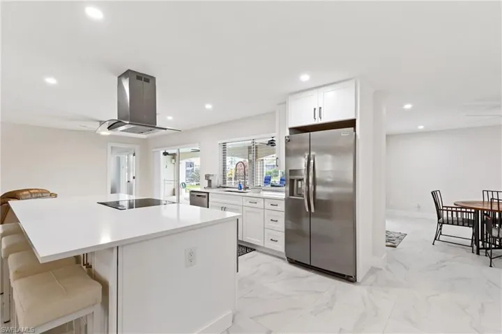 Kitchen with appliances with stainless steel finishes, white cabinets, a breakfast bar, light marble finish floors, and recessed lighting