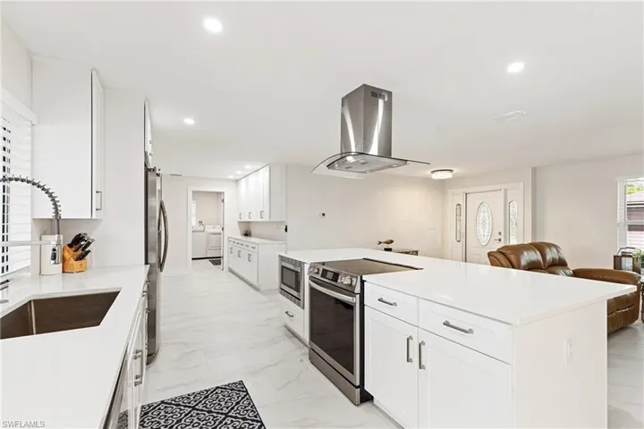 Kitchen featuring appliances with stainless steel finishes, white cabinets, island exhaust hood, light marble finish floors, and recessed lighting