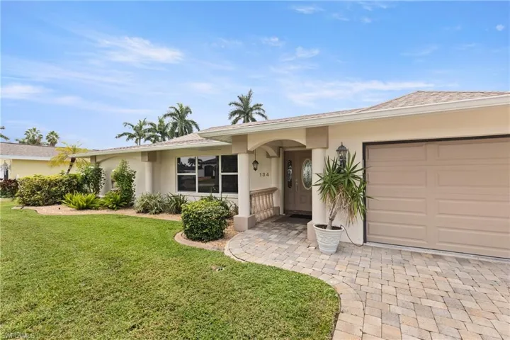 Ranch-style home with stucco siding, a front yard, an attached garage, and decorative driveway