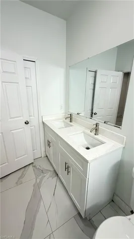 Full bath with double vanity and light marble finish flooring