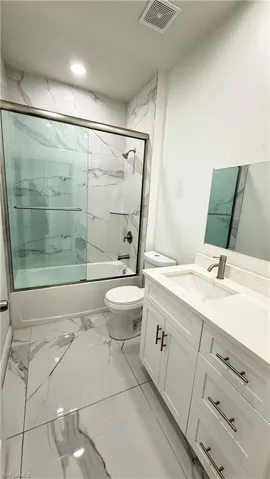 Full bath featuring vanity, bath / shower combo with glass door, and light marble finish flooring