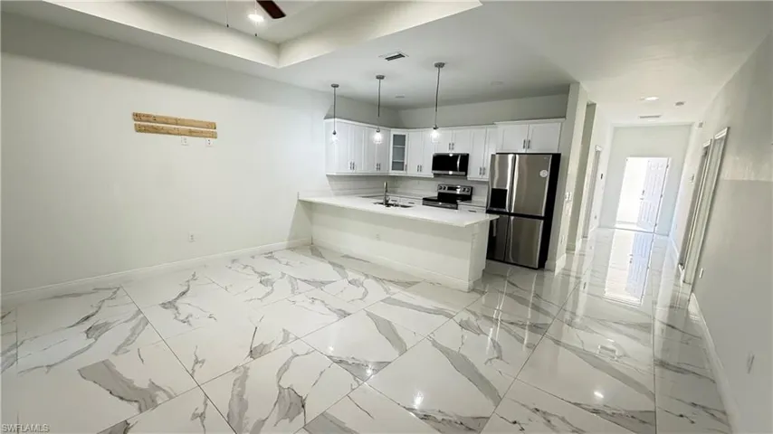 Kitchen featuring stainless steel appliances, white cabinetry, hanging light fixtures, glass insert cabinets, and a peninsula
