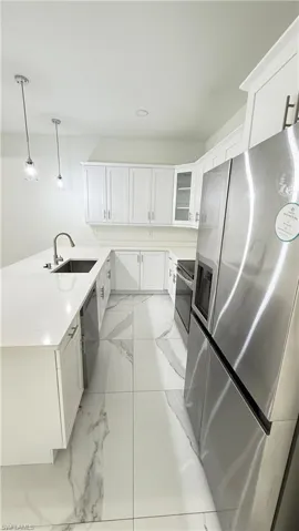 Kitchen featuring white cabinetry, stainless steel appliances, pendant lighting, a peninsula, and glass fronted cabinets