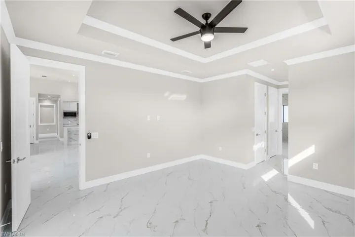 Spare room with a tray ceiling, light marble finish flooring, and ceiling fan