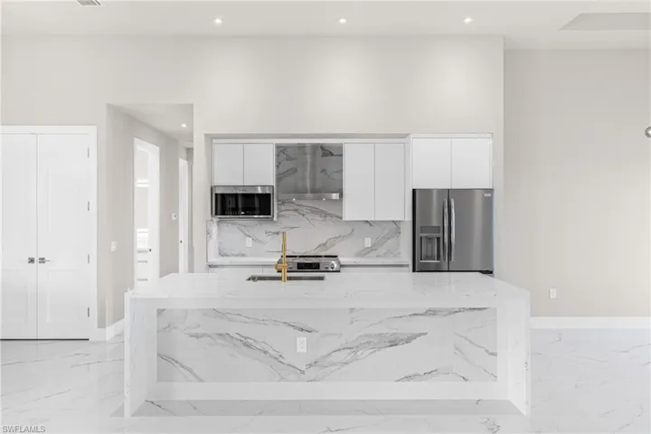 Kitchen featuring light stone countertops, white cabinets, stainless steel appliances, modern cabinets, and wall chimney range hood