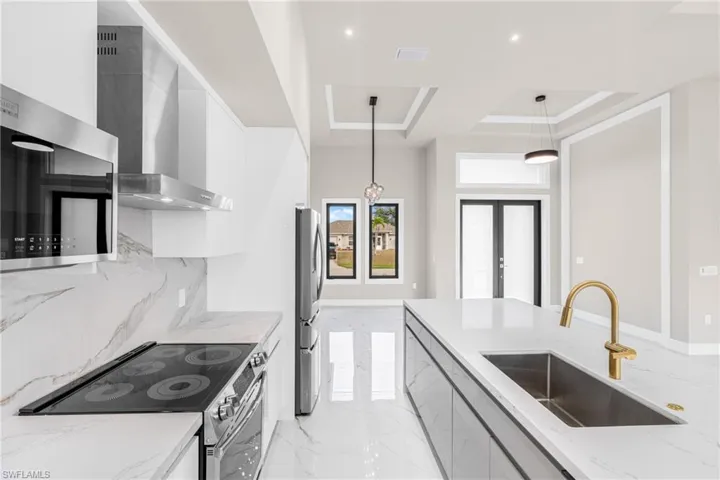 Kitchen with stainless steel appliances, pendant lighting, light marble finish flooring, light stone counters, and wall chimney exhaust hood