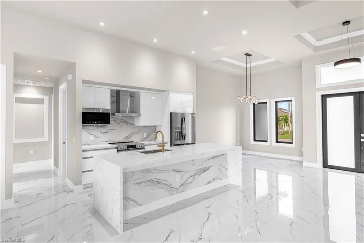 Kitchen with modern cabinets, hanging light fixtures, white cabinetry, light stone counters, and recessed lighting