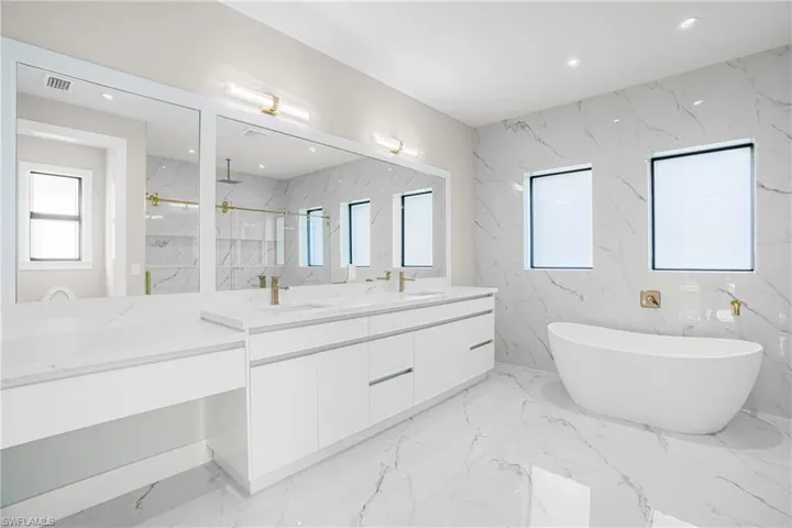 Bathroom with double vanity, a marble finish shower, a freestanding bath, stone wall, and recessed lighting