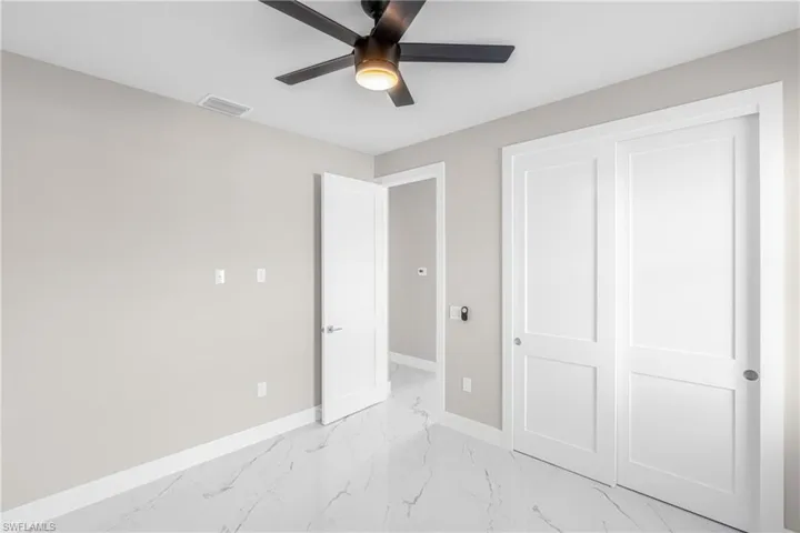 Unfurnished bedroom featuring ceiling fan, light marble finish flooring, and a closet