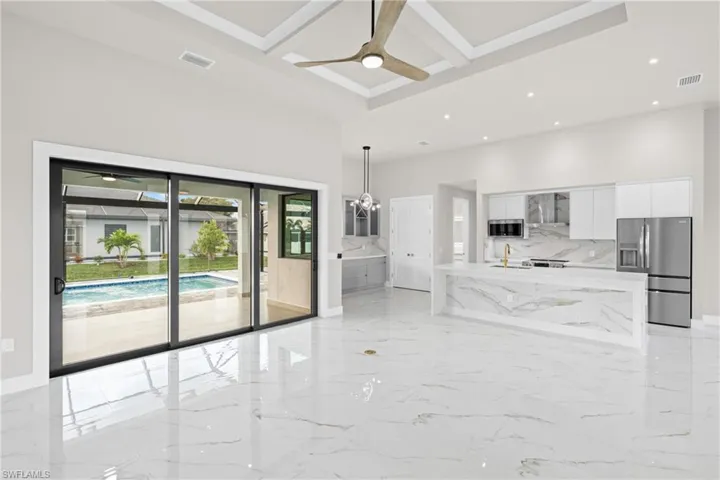 Unfurnished living room with light marble finish flooring, coffered ceiling, a chandelier, ceiling fan, and recessed lighting