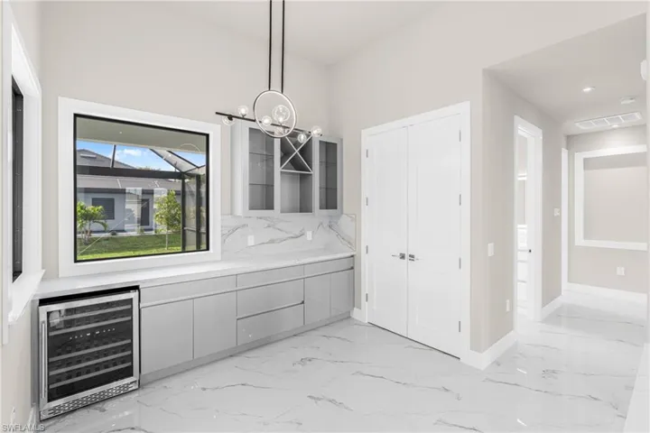 Bar featuring wine cooler, glass insert cabinets, light marble finish flooring, pendant lighting, and gray cabinetry