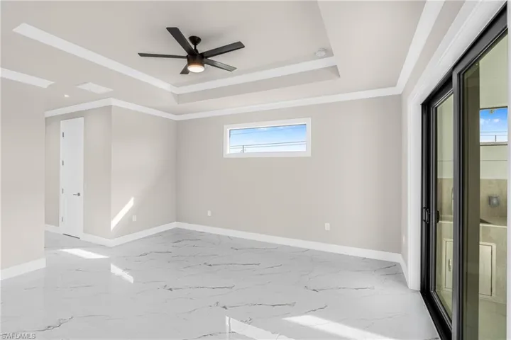 Spare room with light marble finish floors, ornamental molding, a tray ceiling, and ceiling fan