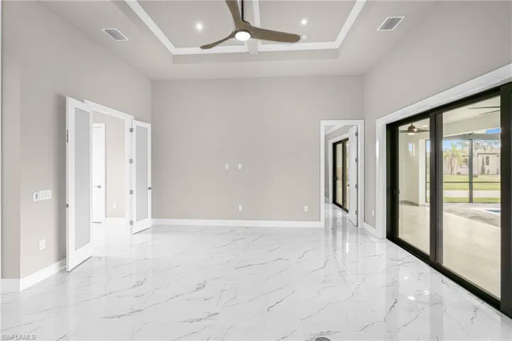 Empty room with light marble finish floors, a ceiling fan, recessed lighting, a tray ceiling, and a towering ceiling