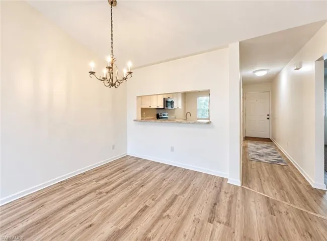 Dining area featuring wood-finish flooring, a multi-arm candelabra chandelier, and a kitchen pass-through with stone-finish countertop