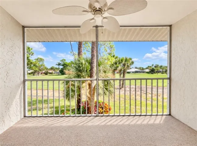 Screened lanai featuring a ceiling fan, textured wall finish, and metal railing overlooking a landscape with mature trees and palms