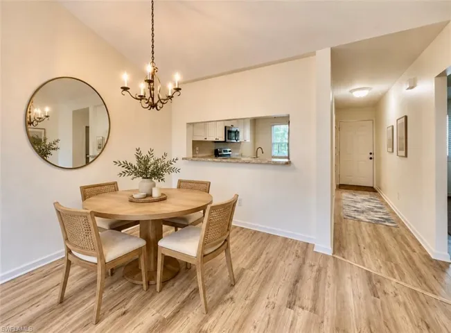 **Virtually staged Dining area featuring wood-finish flooring, a tiered metal chandelier, and a pass-through opening to the kitchen with a stone-surfaced counter