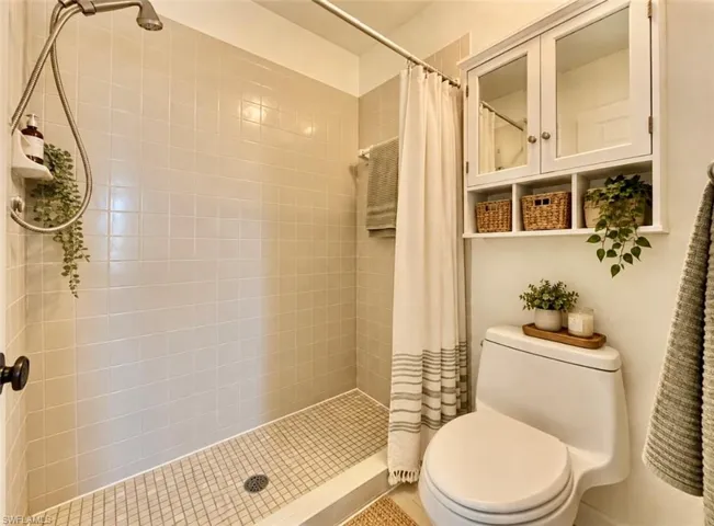 **Virtually staged Tiled walk-in shower with a wall-mounted shower head, white finish toilet, and wall-mounted white cabinetry featuring dual mirrored doors and open shelving
