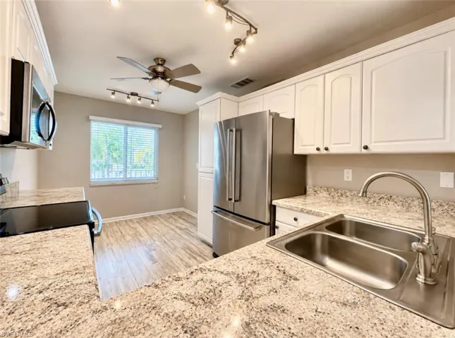 Kitchen featuring white cabinetry, stone-finish countertops, stainless steel appliances, double basin undermount sink, and wood-finish flooring