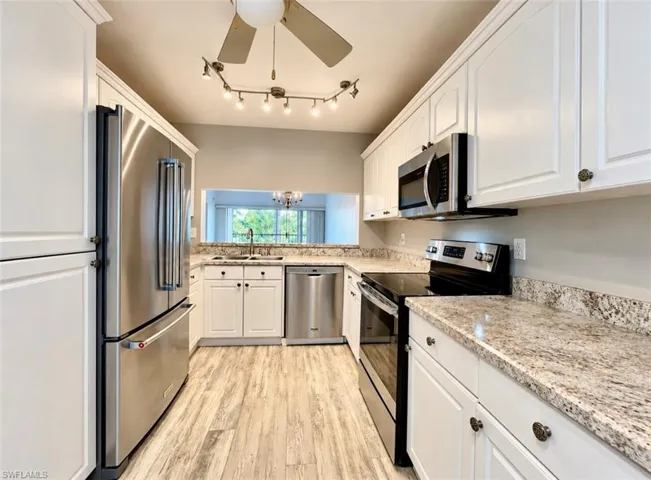 Kitchen featuring white cabinetry, stone-finish countertops, stainless steel appliances, wood-finish flooring, and a ceiling-mounted track lighting fixture
