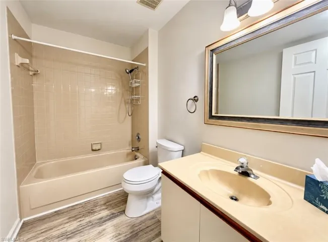 Bathroom featuring wood-finish flooring, a molded vanity countertop with an integrated sink, a tiled tub surround, and a wall-mounted framed mirror