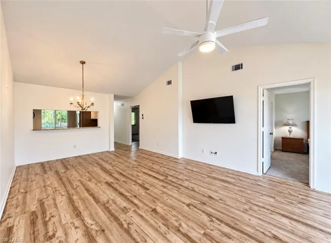 Vaulted ceilings, wood-finish flooring, recessed lighting, ceiling fan with integrated light fixture, and decorative metal chandelier